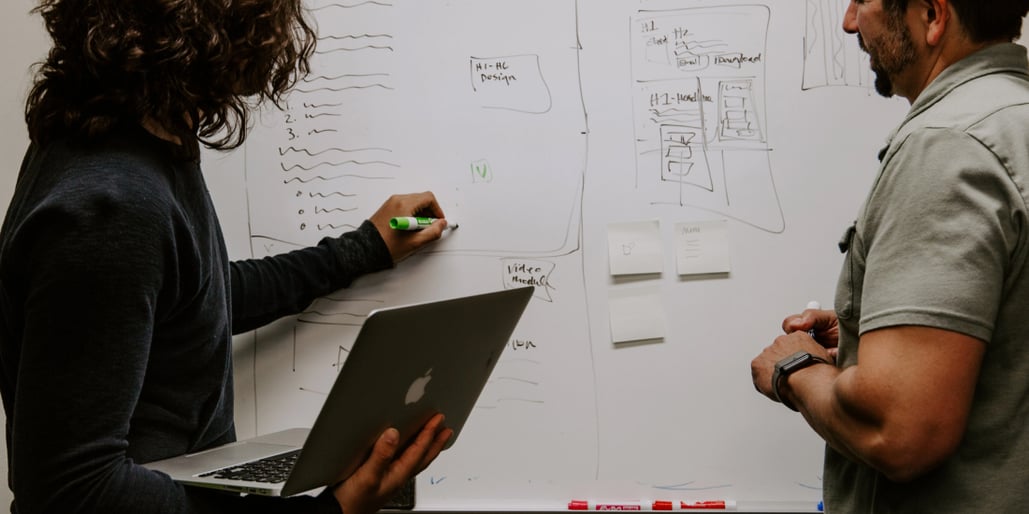 Two people writing on a white board