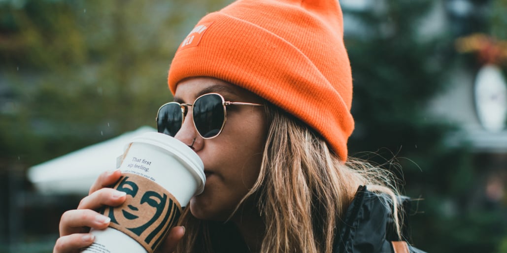 Jente med oransje lue som drikker av pappkrus fra Starbucks